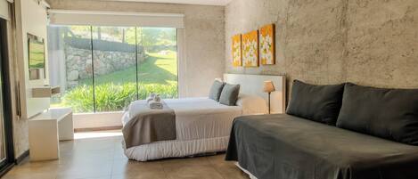 Un dormitorio con cama, sofá, ventana con vistas a follaje y obras de arte en la pared.