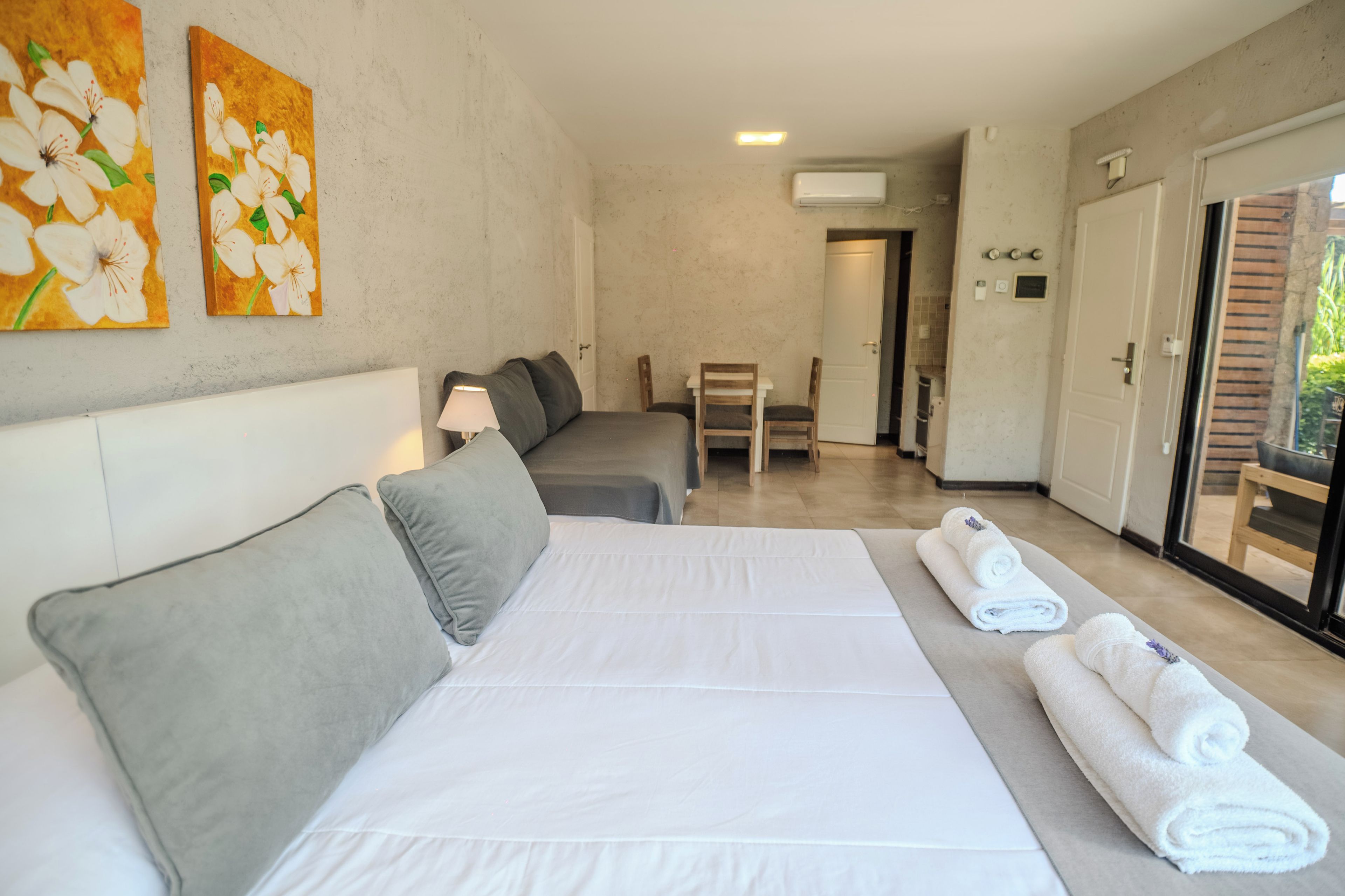 A hotel room with a bed, a desk, and a chair. There are two paintings on the wall.