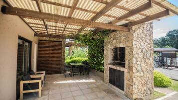 Eine Außenpatio mit Kamin aus Stein, Holzmöbeln und einem überdachten Bereich mit Wellblechdach.