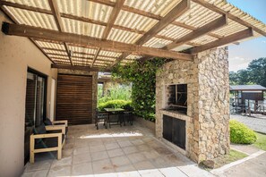 An outdoor patio with a stone fireplace, wooden furniture, and a covered area with a corrugated roof.