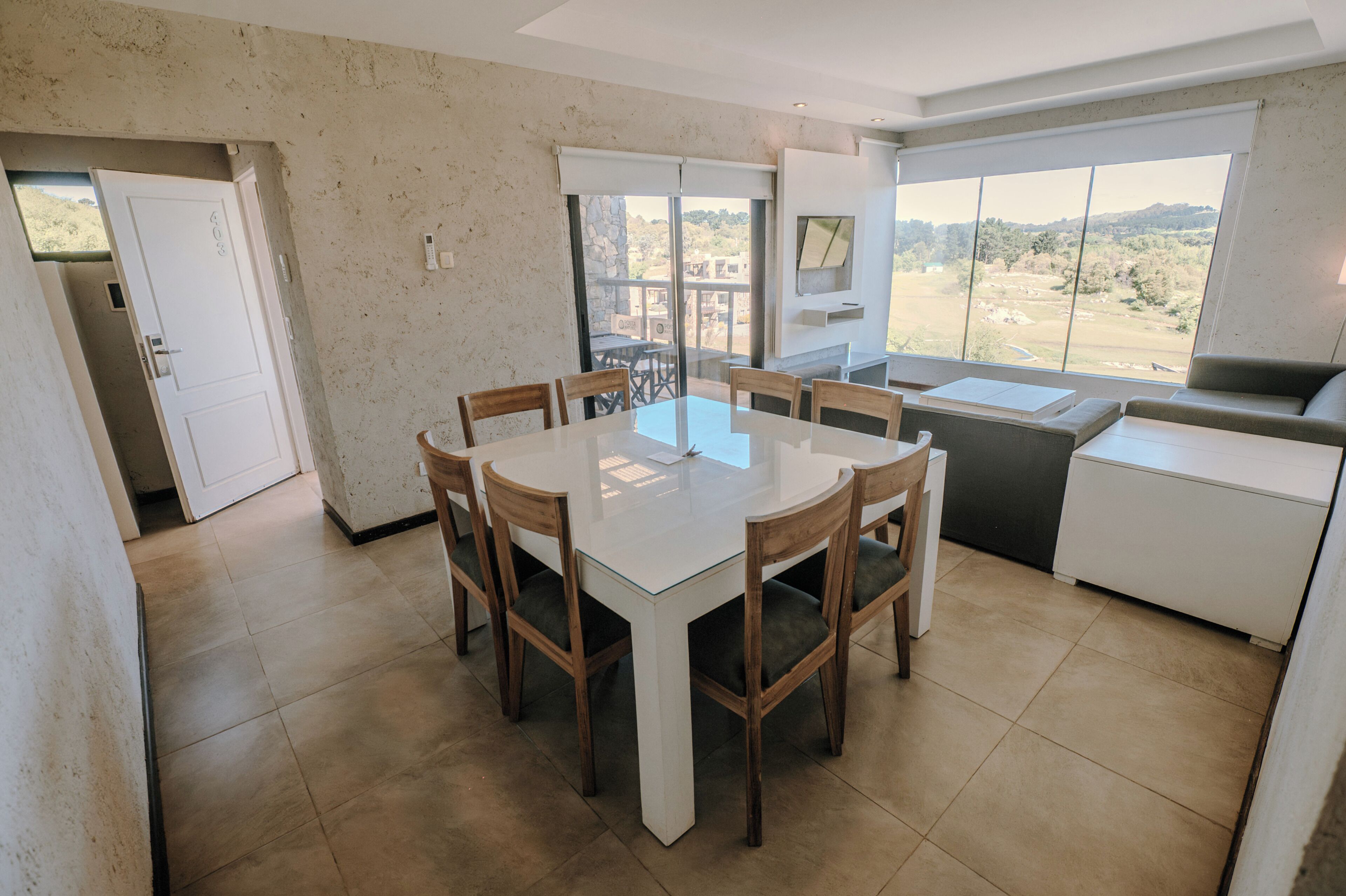 Un comedor con una mesa redonda, sillas de madera y vistas al exterior a través de amplios ventanales.