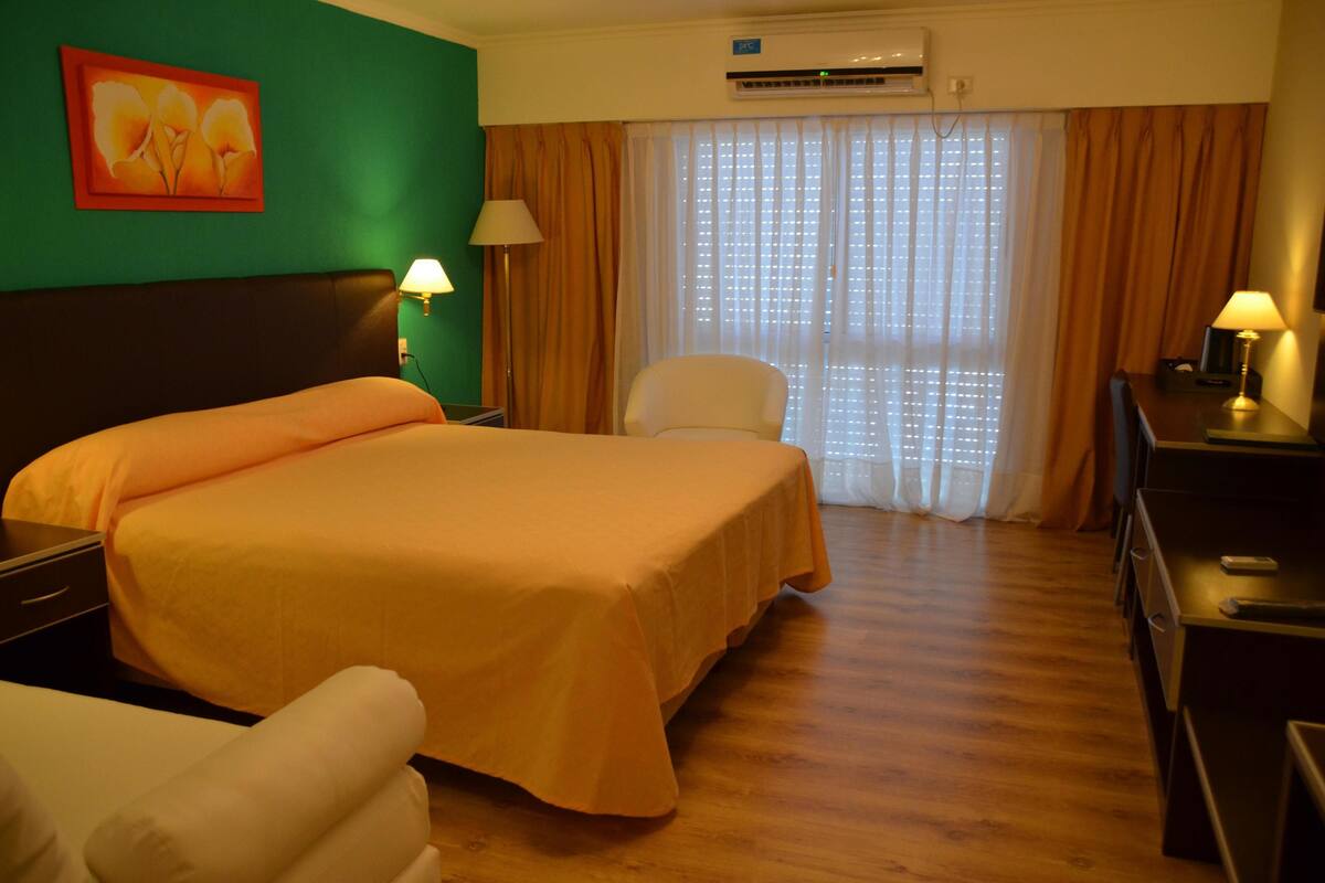 A hotel room with a large bed, a chair, a desk, and a window with curtains.