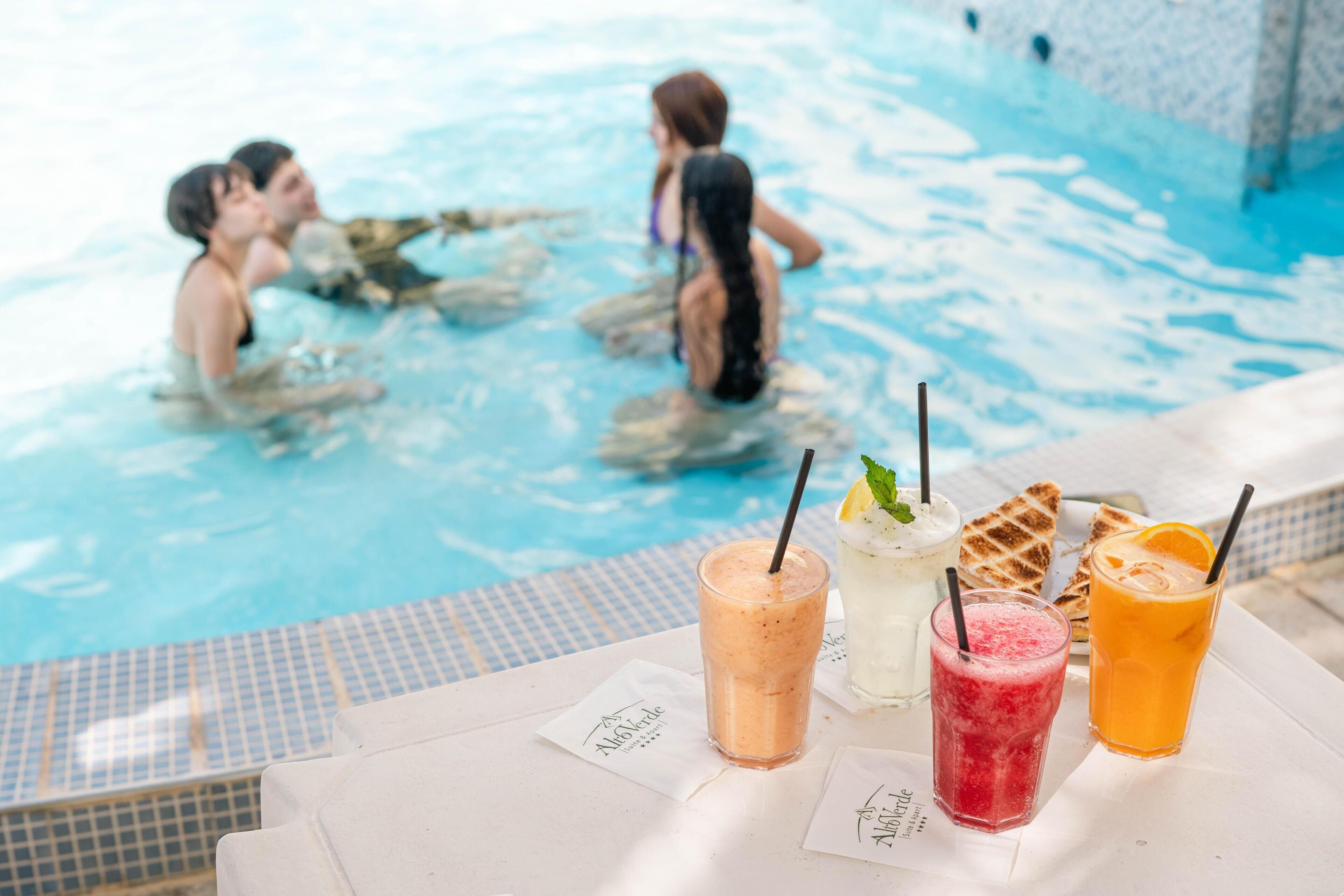 A poolside area with a table displaying various drinks and a tiled pool edge.