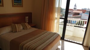 A hotel room with a large bed, a wooden headboard, a nightstand, a lamp, and a view of the outside balcony through a sliding glass door. - Nelson Praia Hotel (Rio Grande)
