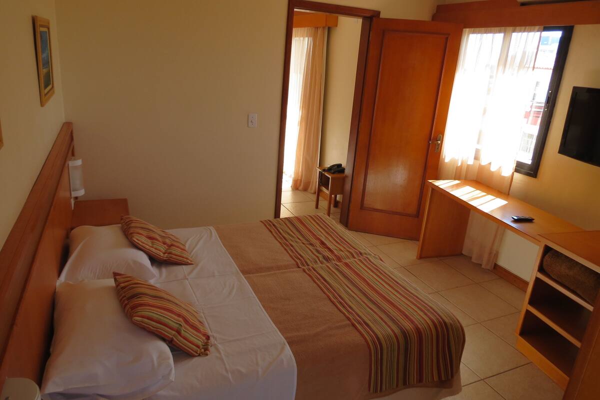 A hotel room with a bed, a desk, a television, and a bathroom visible through an open door.
