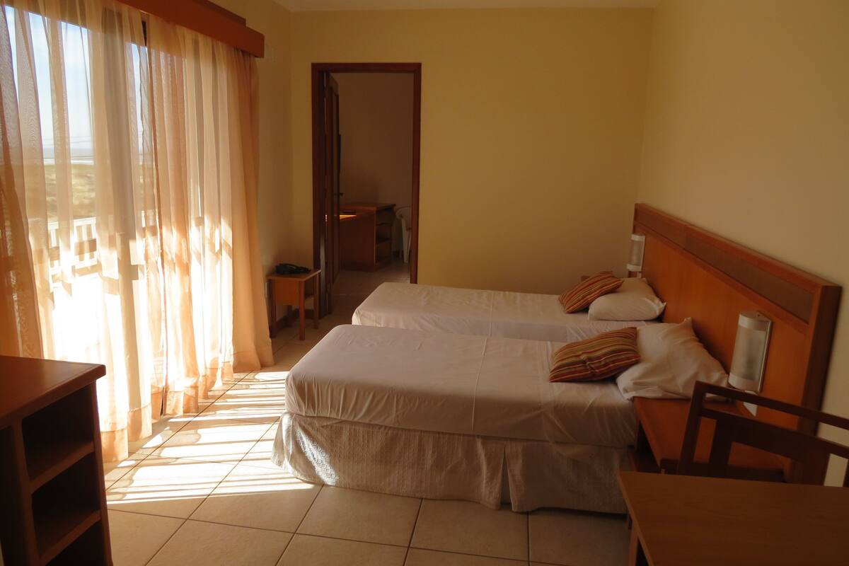 A hotel room with two beds, a wooden headboard, a table, and a chair.