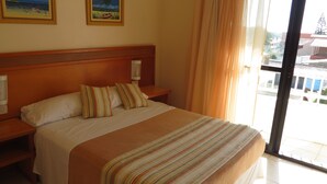 A hotel room with a large bed, two nightstands, a window with curtains, and two framed pictures on the wall. - Nelson Praia Hotel (Rio Grande)