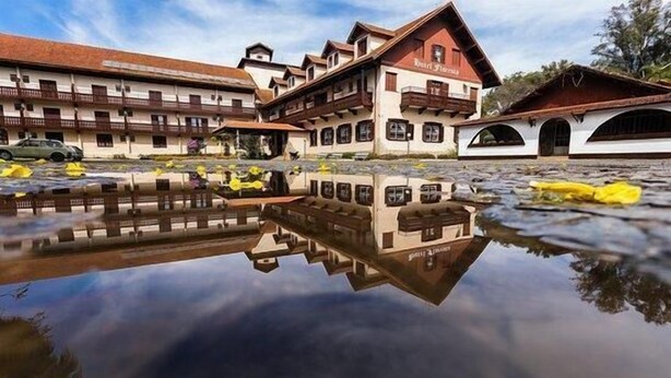 A building with a reflection in the water, featuring balconies and a red roof. - Hotel Floresta (Poços de Caldas)
