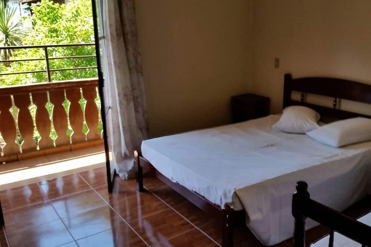 Un dormitorio con una cama, una mesita de noche y vistas a la vegetación a través de una ventana.