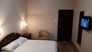 A hotel room with a bed, a chair, a TV, and a door. - Hotel Floresta (Poços de Caldas)