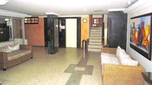 A lobby with two wicker sofas, a marble column, a staircase, and a painting on the wall. - Apartamento Arena - Smr236a (Santa Marta)