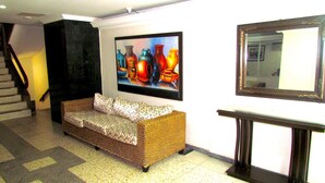 A lobby with a patterned sofa, a staircase, a framed painting, and a mirror. - Apartamento Arena - Smr236a (Santa Marta)