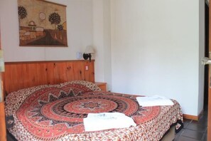 A bedroom with a round bed, a wooden headboard, a wall painting, and a bedside lamp.