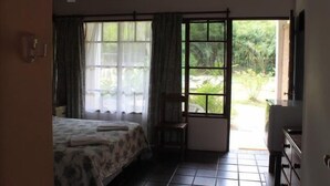 A bedroom with a bed, a chair, a desk, and a window with a view of greenery. - Hotel La Ballena (Punta del Este)