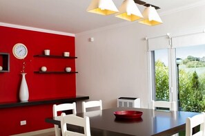 A modern dining area with a red accent wall, white chairs, a black table, and a red bowl.
