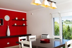 Un área de comedor moderna con una pared de acento roja, sillas blancas, una mesa negra y un cuenco rojo.