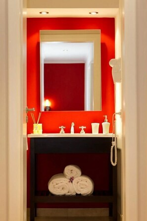 A bathroom with a red wall, a white sink, a mirror, a telephone, and towels on a shelf.