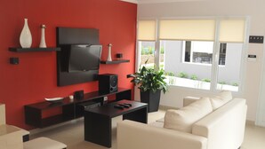 Un salon moderne avec un mur d’accent rouge, un téléviseur à écran plat, un meuble de rangement noir, un canapé beige, une table basse et une plante en pot.