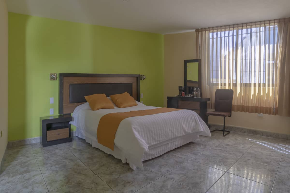 A hotel room with a bed, nightstands, a chair, a desk, and a window with curtains.