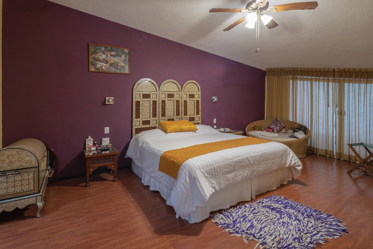 A bedroom with a bed, a nightstand, a chair, a ceiling fan, and a window with curtains.