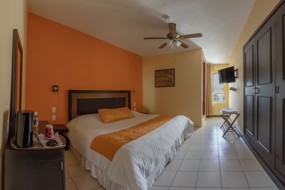 A hotel room with a bed, a ceiling fan, a TV, and a wardrobe.