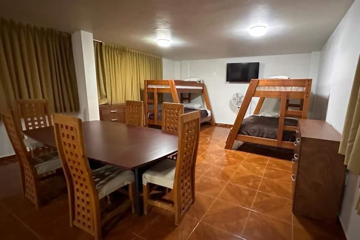 A room with a wooden dining table, chairs, bunk beds, a TV, and a fan.