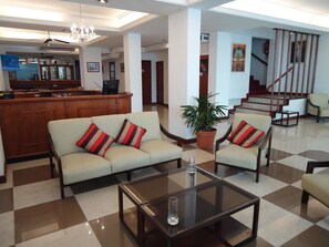 A spacious lobby with a checkered floor, a sofa set with striped cushions, a coffee table, and a potted plant.