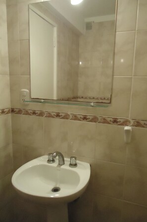 A bathroom with a white sink, a glass shelf above it, and a mirror.