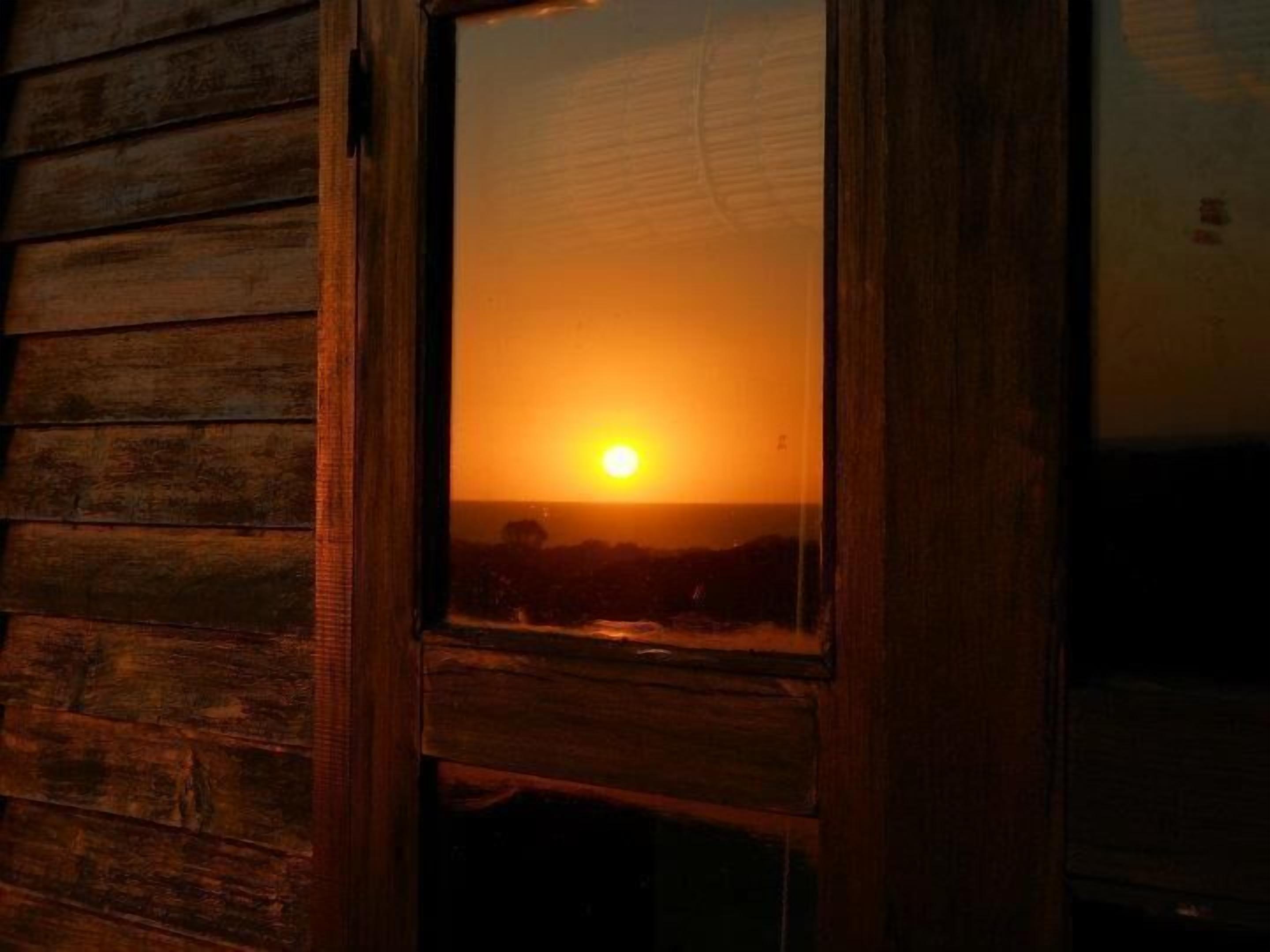 A wooden cabin with a window reflecting a sunset.