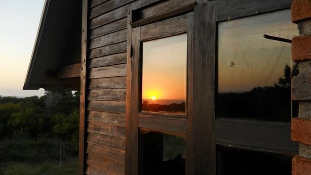 Eine Holzhütte mit einem Fenster, das einen Sonnenuntergang widerspiegelt.