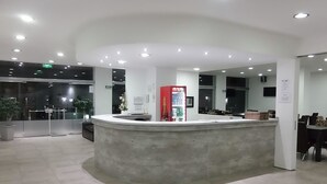 A reception area with a curved counter, a red beverage dispenser, and a glass door entrance. - Pinar del Lago (Villa Carlos Paz)