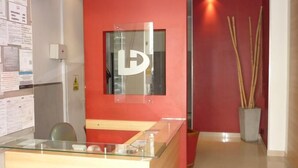 A reception area with a glass desk, a red wall, and a sign with a letter 'D'. - Du Helder (Buenos Aires)