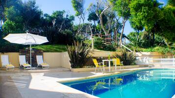 A swimming pool with a clear blue water, surrounded by a patio area with yellow chairs and a table.