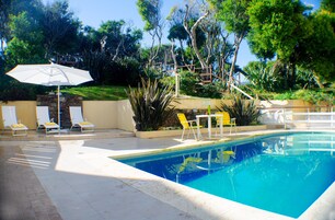 A swimming pool with a clear blue water, surrounded by a patio area with yellow chairs and a table.