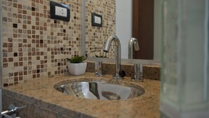 Baño con lavamanos, espejo y salpicadero de mosaicos.