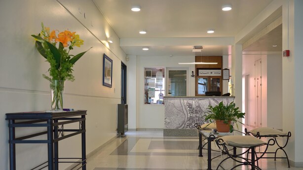 Un vestíbulo de hotel con una recepción, una zona de estar con una mesa y sillas, una planta en maceta y un cuadro en la pared.