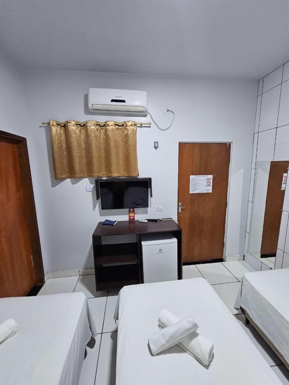 A hotel room with a bed, a desk with a computer, a television, and an air conditioning unit.