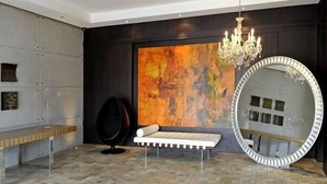 A modern room with a large abstract painting, a round mirror, a bench, and a chandelier. - Ritz Plaza Suite (Quito)