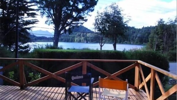 A wooden deck with two chairs, overlooking a lake and trees. - Monoambiente del Trebol (San Carlos de Bariloche)