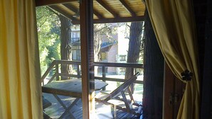 A wooden deck with a bench and a table, surrounded by trees and a brick building. - Alma del Monte (Mar de las Pampas)