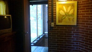 A room with a brick wall, a framed painting, a television on a wooden stand, and a window with blinds. - Alma del Monte (Mar de las Pampas)