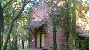 A rustic brick building with a wooden porch, surrounded by trees and natural vegetation. - Alma del Monte (Mar de las Pampas)