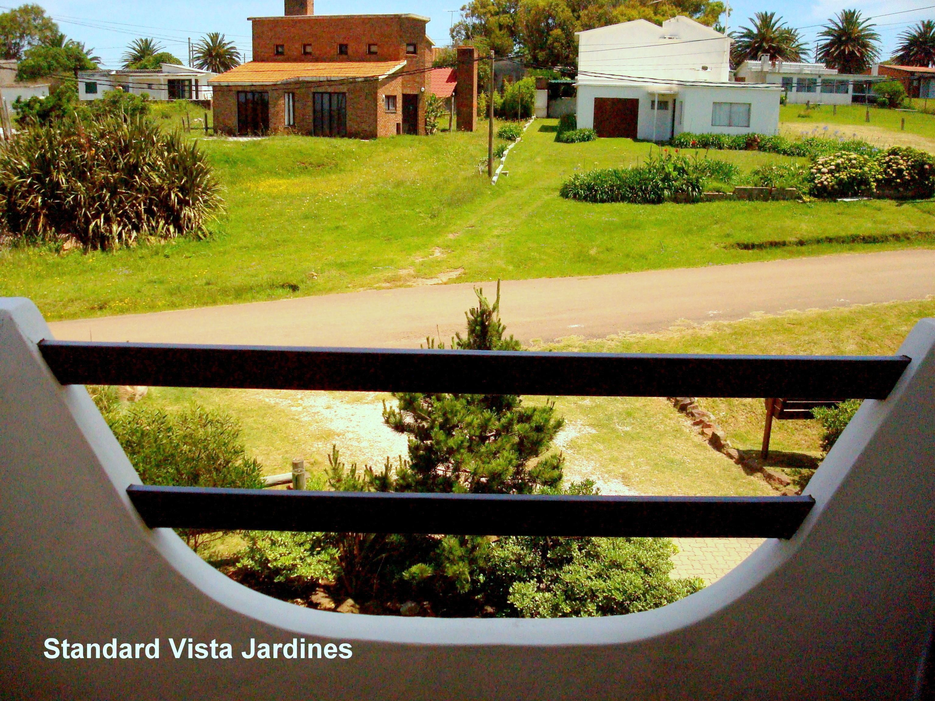 A view of Standard Vista Jardines with a paved driveway, green lawns, and residential buildings in the background.