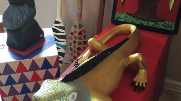 Una escultura colorida de un lagarto sobre un pedestal rojo, rodeada de diversos objetos decorativos, incluyendo un cuadro enmarcado y una escultura verde.