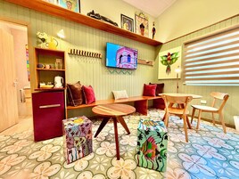 Una habitación con un banco de madera, una mesita pequeña, un televisor montado en la pared y un suelo con diseño.