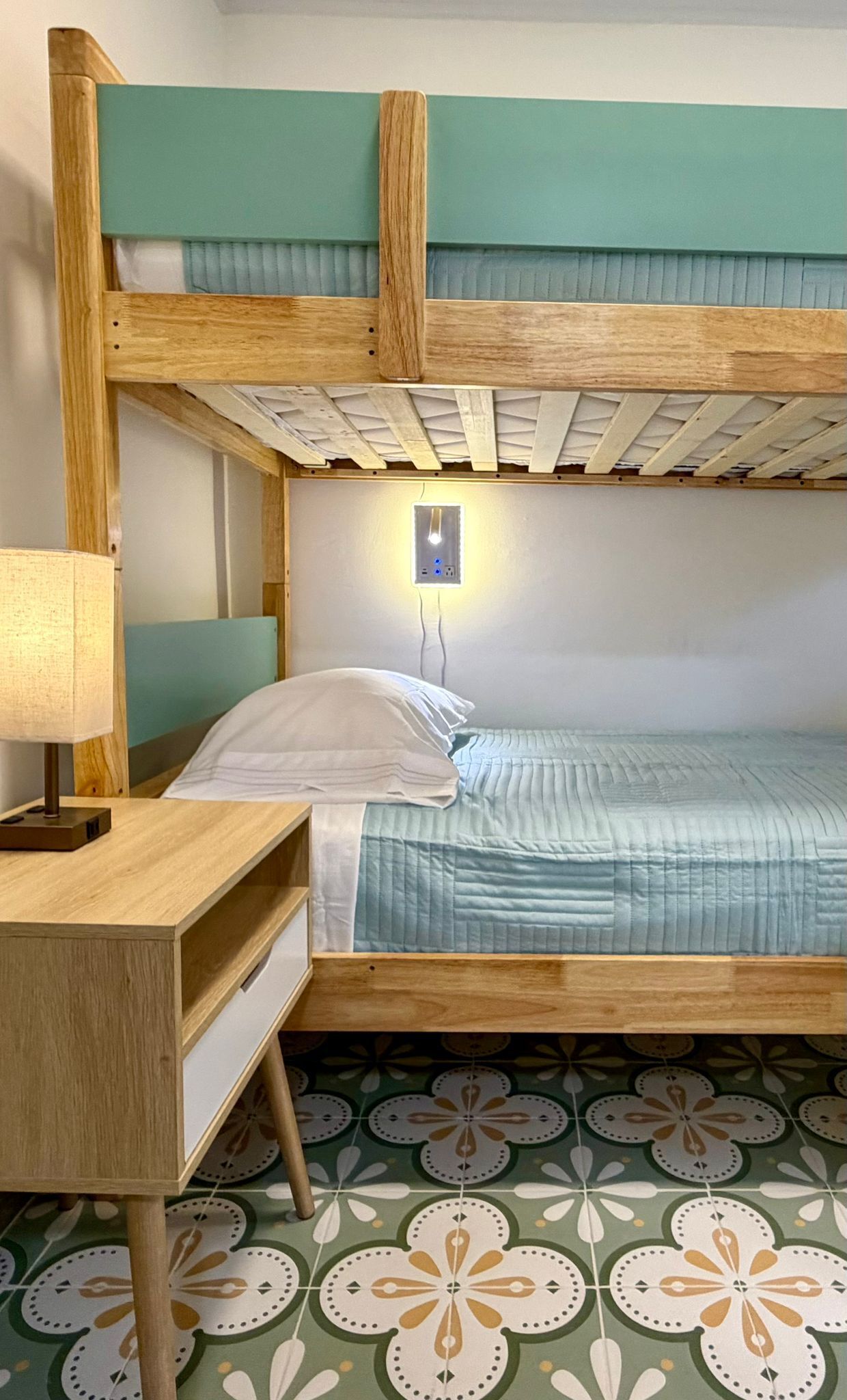 A bunk bed with a desk and lamp, a wall socket, and patterned floor tiles.