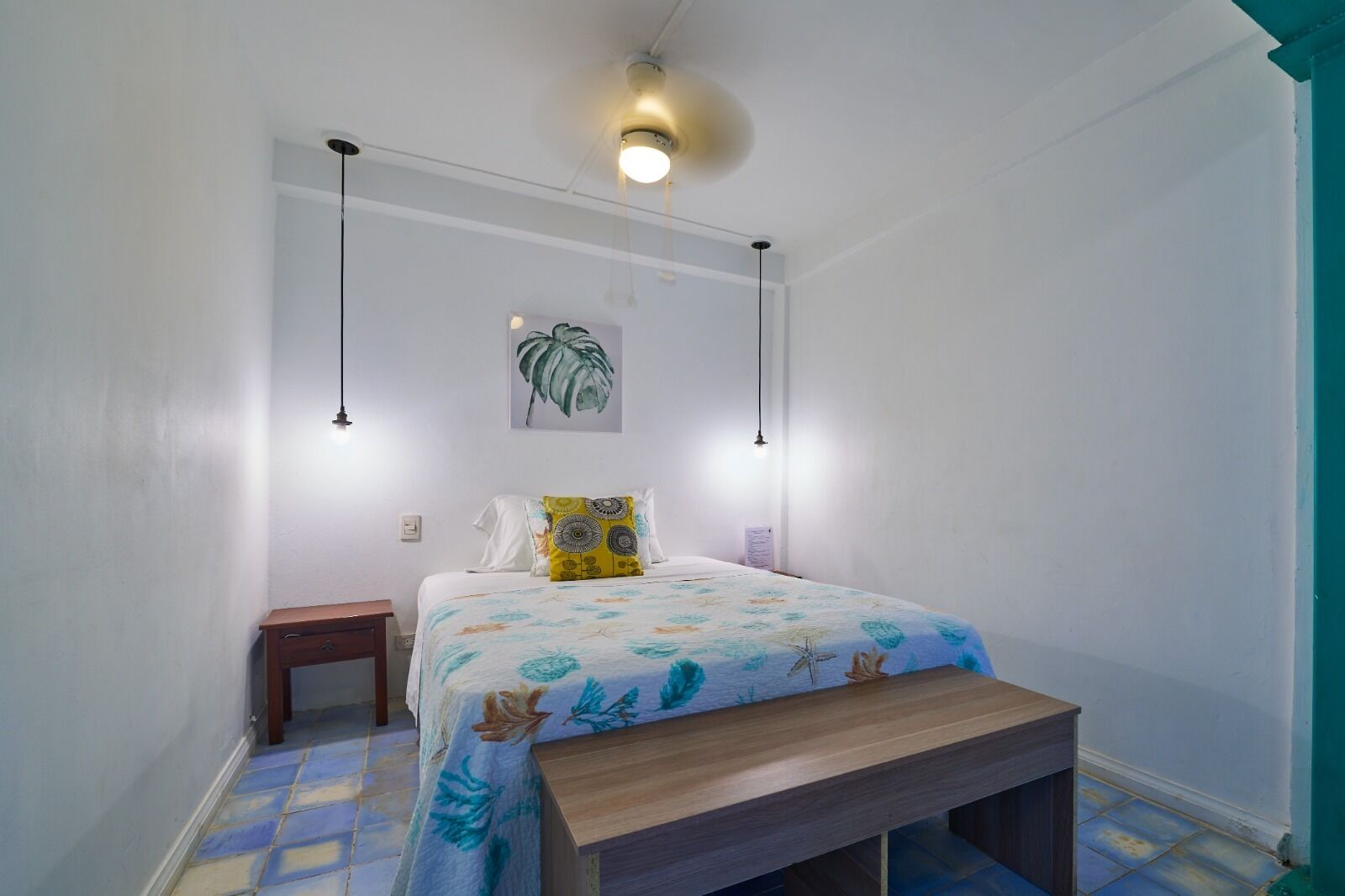 A bedroom with a bed, bedside table, bench, and pendant lights.