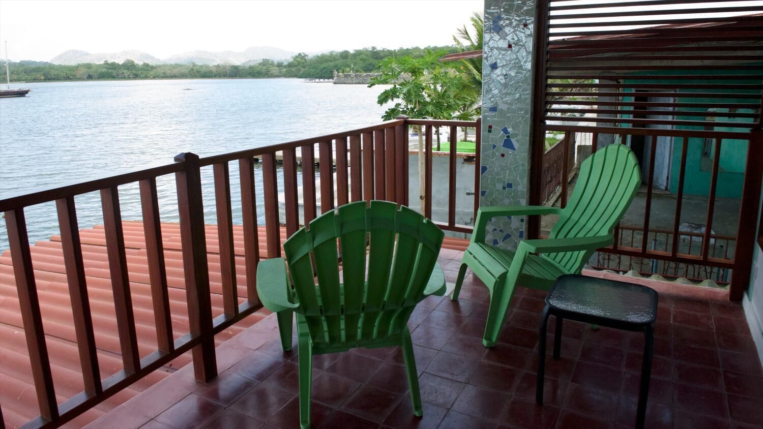 Un balcon donnant sur un lac, deux chaises vertes et une petite table.