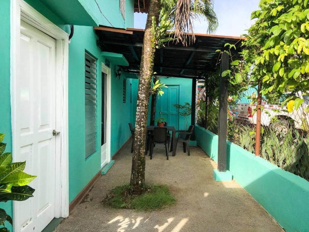 A covered outdoor area with a table and chairs, a door, and a small tree.