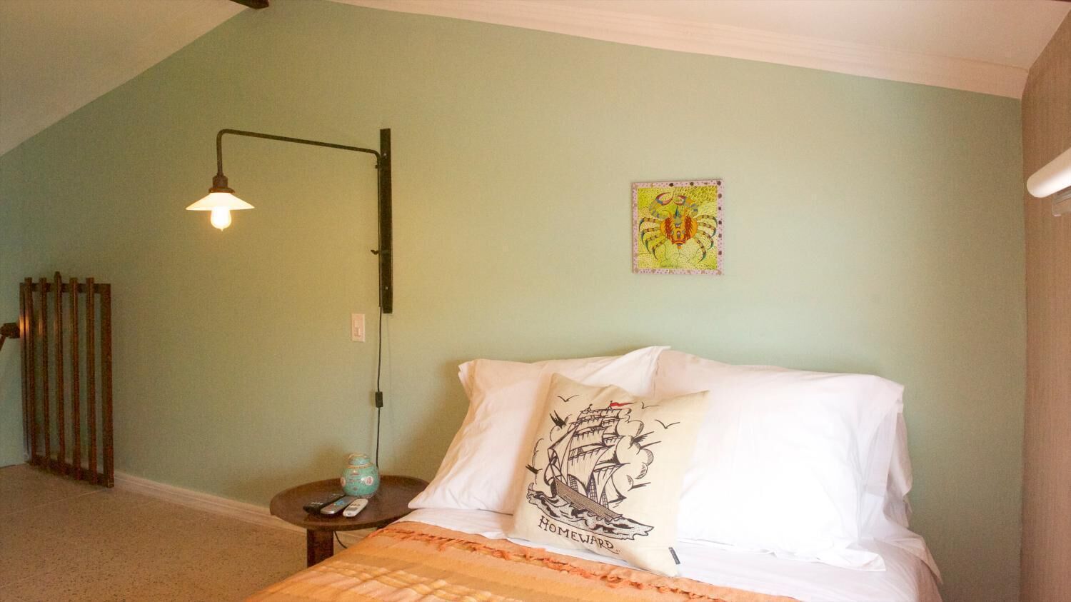 A bedroom with a bed, a nightstand, a lamp, a wall clock, and a framed picture.